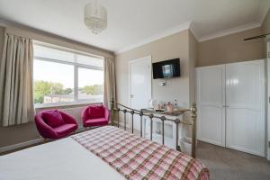 a bedroom with a bed and two pink chairs at The Coast Yard B & B and Garden Chalets in Chichester