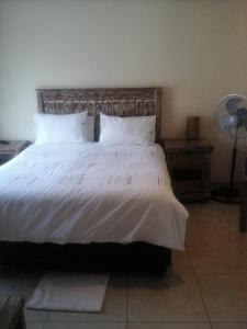1 dormitorio con 1 cama grande con sábanas y almohadas blancas en Koiketla Guesthouse, en Pretoria