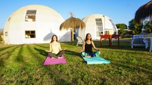two women sitting in the grass doing yoga in front of domes at Hotel Domos Dream in La Serena