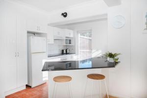 a white kitchen with a black counter and two stools at Denhams Beach side holiday apartment in Batemans Bay +32 photos