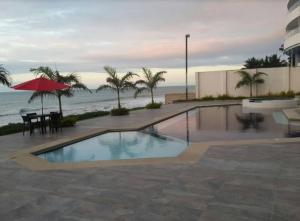 a swimming pool with a table and an umbrella and the ocean at Dpto Moderno Frente al Mar. Edf: Deymar 7mo Piso in Tonsupa