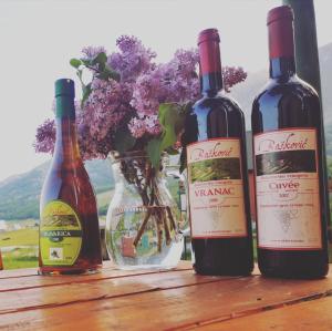 three bottles of wine on a wooden table with a vase of flowers at Guest House Tiha noć in Žabljak