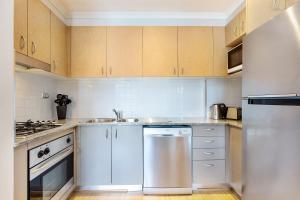 La cuisine est équipée de placards blancs et d'un réfrigérateur en acier inoxydable. dans l'établissement 1 bdrm Surry Hills - Super central location -1012 ELZ, à Sydney