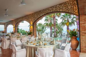 une salle de banquet avec des tables blanches, des chaises et des palmiers dans l'établissement Hotel Olimpo le Terrazze, à Letojanni