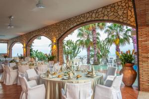 a banquet hall with white tables and chairs and palm trees at Hotel Olimpo le Terrazze in Letojanni +37 photos