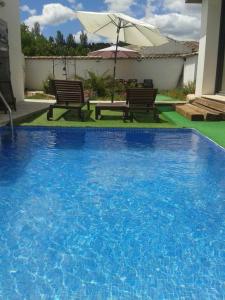 a large blue swimming pool with two benches and an umbrella at Casa Oretani in Picón