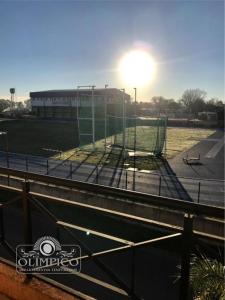 uma gaiola de rebatidas em frente a um edifício com o sol em OLÍMPICO em Concepción del Uruguay