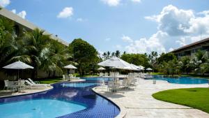 una piscina del complejo con mesas, sillas y sombrillas en Carneiros Beach Resort en Praia dos Carneiros