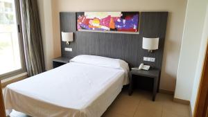Habitación de hotel con cama blanca y teléfono en Alcocebre Suites Hotel en Alcossebre