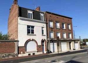 un ancien bâtiment en briques avec deux portes de garage blanches dans l'établissement Apparthotel Douai Gare, à Douai