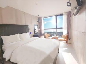 ein weißes Bett in einem Zimmer mit einem großen Fenster in der Unterkunft Hotel Stay Interview Jeju in Seogwipo