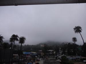 a misty mountain with palm trees and a city at Hotel Kiran in Mount Ābu