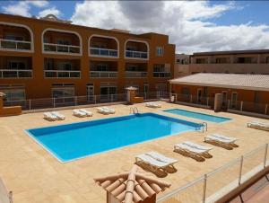 a hotel with a swimming pool and chairs and a building at Cotillo Beach & Sport in Cotillo