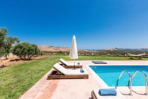 a swimming pool with an umbrella and chairs next to at Dimokritos Villas IV, V, & VI, a homestay experience, By ThinkVilla in Angeliana