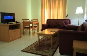 Al Shorouq Hotel Apartments في مسقط: غرفة معيشة مع أريكة وطاولة وتلفزيون