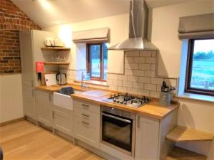 La cuisine est équipée de placards blancs et d'un four avec plaques de cuisson. dans l'établissement Blashford Manor Holiday Cottage - The Dartmoor Cottage, à Ellingham
