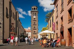 a group of people sitting at tables on a street with a clock tower at La Laguna Luxe Apartment in La Laguna