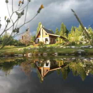 a house is reflected in the water of a lake at Del Viejo Camino in El Bolsón