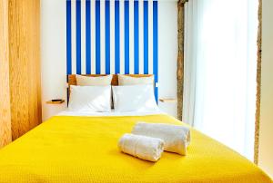 uma cama com um cobertor amarelo e duas toalhas em Almar Apartments na Póvoa do Varzim