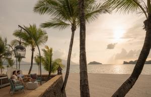 two people sitting in chairs on the beach with palm trees at Four Seasons Resort Langkawi in Tanjung Rhu