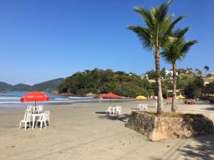 einen Strand mit Liegestühlen und Sonnenschirmen und einer Palme in der Unterkunft Cond Apartamentos Chalés San Marino in Ubatuba