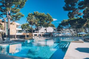 a swimming pool with chairs and trees in a resort at Iberostar Selection Playa de Muro Village in Playa de Muro