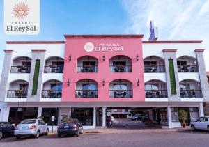 różowy budynek z samochodami zaparkowanymi przed nim w obiekcie Hotel Posada El Rey Sol w mieście Ensenada