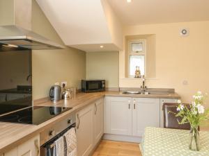 a kitchen with white cabinets and a sink and a microwave at Ferngrove Cottage in Bishop Auckland