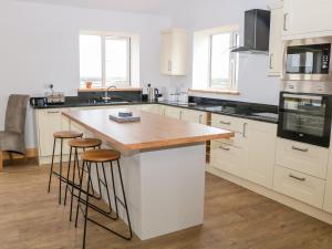 a kitchen with white cabinets and a wooden island with stools at Teal Cottage in Melton Mowbray