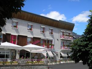 a hotel with tables and umbrellas in front of it at Hôtel Restaurant Le Grillon in Chambon-sur-Lac