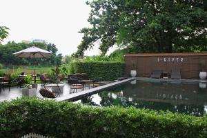 a pool in a garden with chairs and an umbrella at i-river chiangmai in Chiang Mai