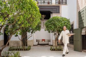 a man holding a plate in a courtyard with trees at Le Farnatchi in Marrakesh