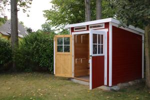 a red shed with a door in a yard at Ferienwohnung Moewennest mit Terra in Middelhagen