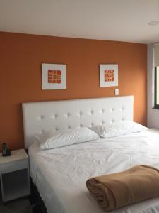 ein Schlafzimmer mit einem weißen Bett und einer orangefarbenen Wand in der Unterkunft Hotel Garden City Boutique in Fusagasuga