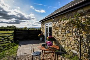 eine Terrasse mit einem Tisch und Stühlen neben einem Steingebäude in der Unterkunft The Hideaway with hot tub in Chathill