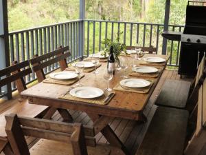 een houten tafel met borden en wijnglazen op een terras bij Treehouse - 3 acre elevated nature setting in Quindalup