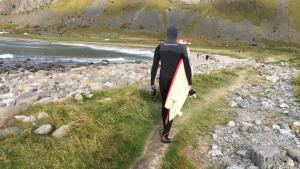un hombre está caminando por un camino con una tabla de surf en Lofoten Fjord Lodge en Saupstad