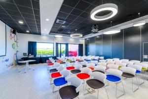 Kyriad Prestige Amiens Poulainville - Hotel and Spa في Poulainville: قاعة المؤتمرات مع الكراسي البيضاء والكراسي الزرقاء