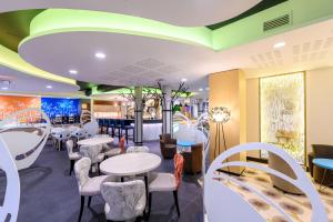 a restaurant with white tables and chairs and a green ceiling at Kyriad Prestige Amiens Poulainville - Hotel and Spa in Poulainville