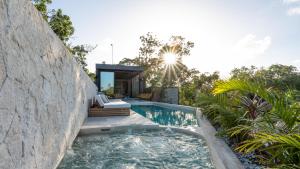 a swimming pool with a stone wall next to a house at Villa LaGú in Tulum