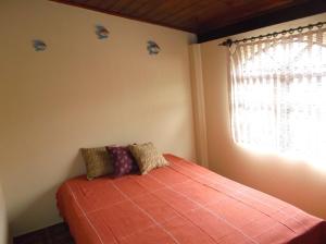 1 dormitorio con 1 cama con manta naranja y ventana en Chalé Barra Velha, en Ilhabela