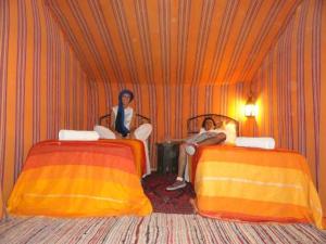Dos mujeres sentadas en una habitación con dos camas. en Visit Morocco Sahara Camp, en Merzouga