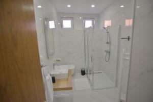 La salle de bains blanche est pourvue d'une douche et d'un lavabo. dans l'établissement Apartman LENA, à Ðakovo