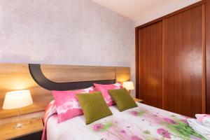 ラ・レスティンガにあるHome2Book Charming Apartment & Diving La Restingaのベッドルーム1室(ピンクと緑の枕が付いたベッド1台付)