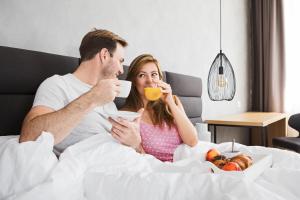 mężczyzna i kobieta siedzący w łóżku pijący kawę i jedzący w obiekcie Korpa Deli Rooms w Nowym Sadzie
