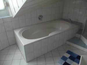 La salle de bains carrelée de blanc est pourvue d'une baignoire et d'une fenêtre. dans l'établissement Ferienwohnung in Puschendorf, à Puschendorf