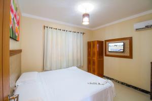 um quarto com uma cama branca e uma televisão em Vila Miola Hotel em Porto Seguro