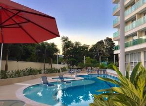 a swimming pool with a red umbrella and chairs and a building at RioStay Residence, Riocentro in Rio de Janeiro