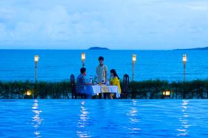 a group of people sitting at a table by a pool at Hon Rom Central Beach Resort in Mui Ne