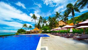 a swimming pool with chairs and umbrellas and the ocean at Hon Rom Central Beach Resort in Mui Ne